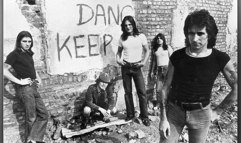 1977:  Promotional portrait of Australian hard-rock group AC/DC standing in front of a graffiti-covered brick wall, (L-R:) dr