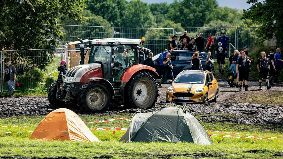 A tractor pulls a car to a parking lot on the muddy festival grounds ahead of the opening of the Wacken Open Air music festiv