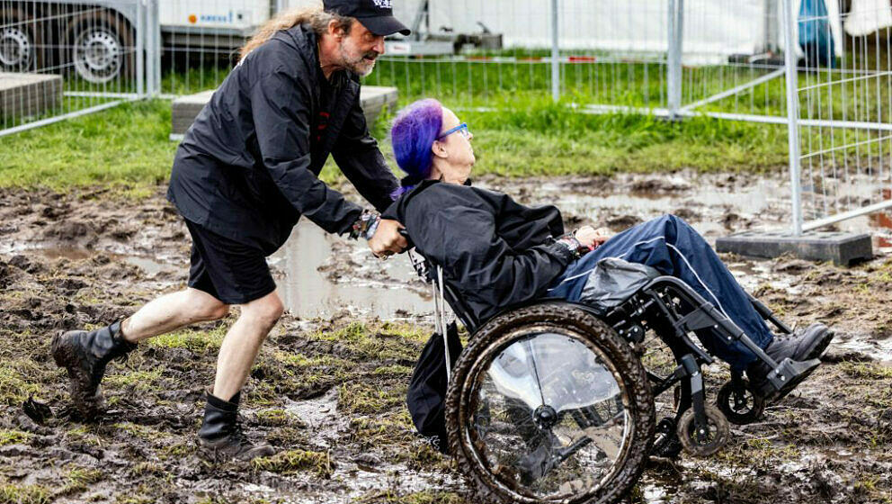 A visitor of the Wacken Open Air in a wheelchair is pushed through the mud at the festival ground on August 1, 2023. Wacken O
